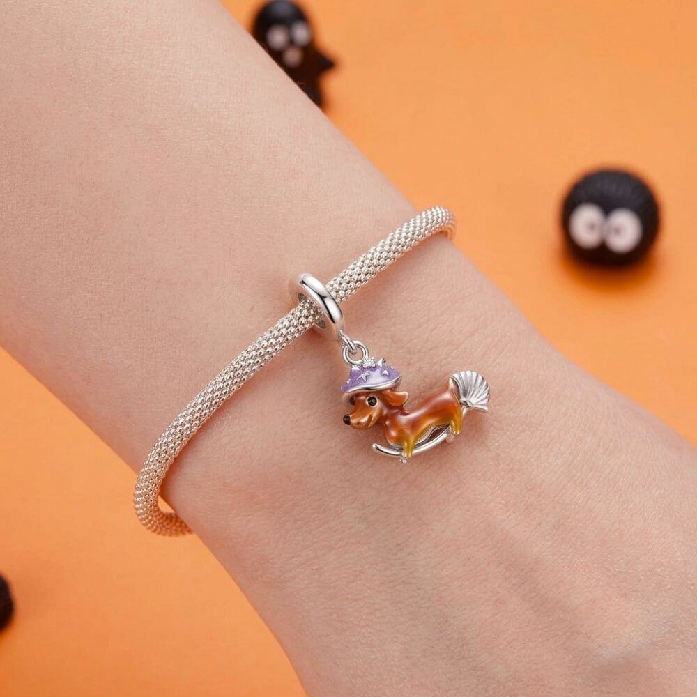 Sterling silver dachshund witch charm with purple hat, broomstick, and playful Halloween details.