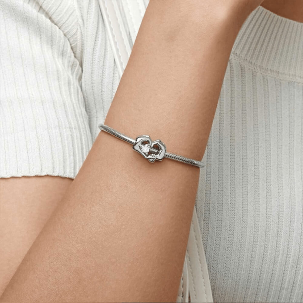 Sterling silver charm with adult and child hands forming a heart around a pink crystal 