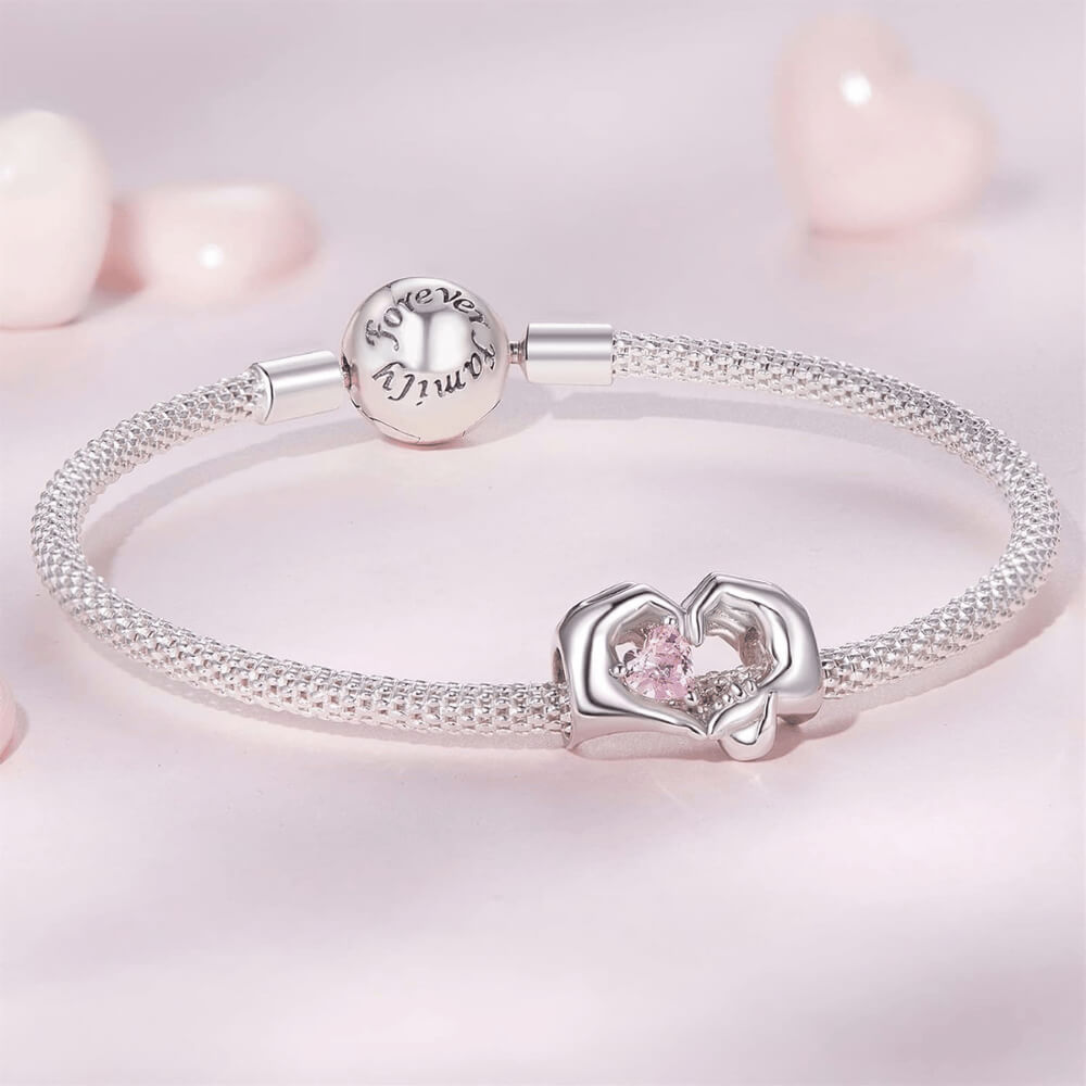 Sterling silver charm with adult and child hands forming a heart around a pink crystal