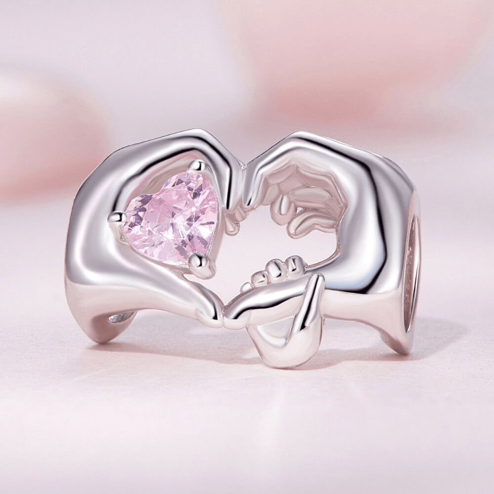 Sterling silver charm with adult and child hands forming a heart around a pink crystal 