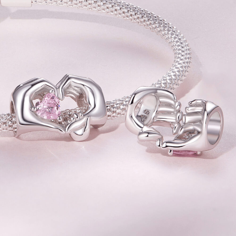 Sterling silver charm with adult and child hands forming a heart around a pink crystal 
