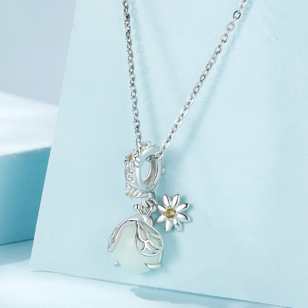 Sterling silver firefly charm with mint glowing enamel body and yellow flower detail.