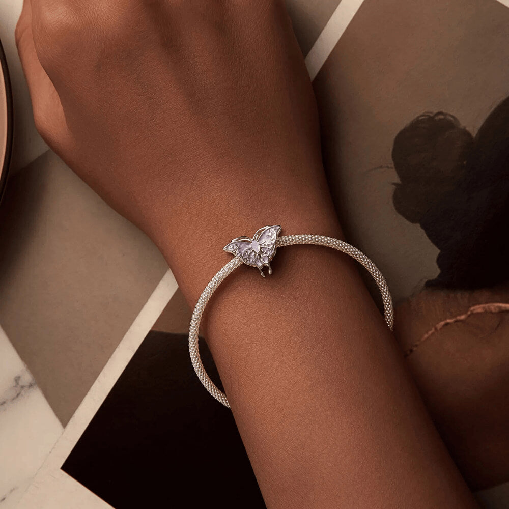 Sterling silver butterfly charm with lavender enamel wings, leaf-shaped filigree details, and an opal-like central gemstone
