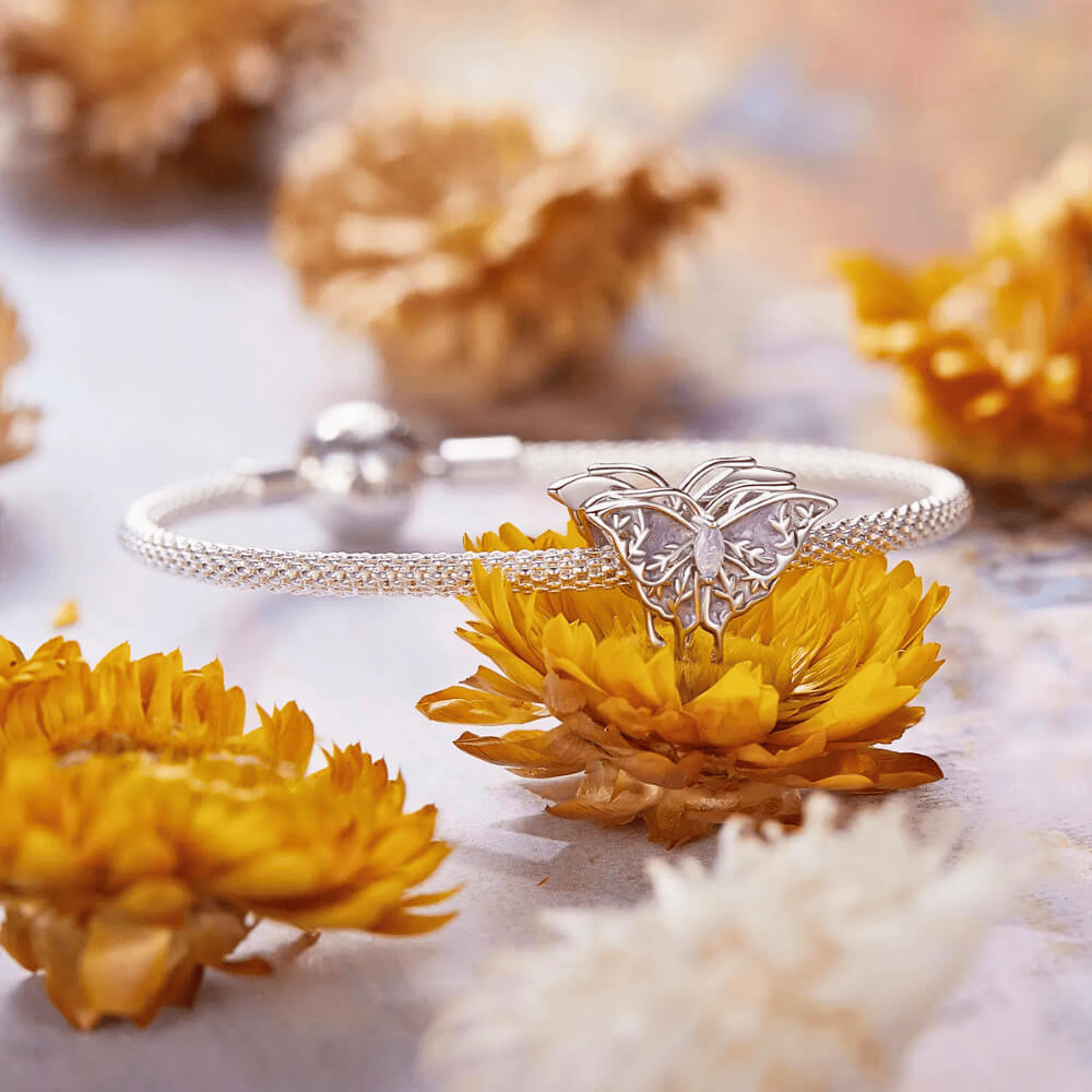 Sterling silver butterfly charm with lavender enamel wings, leaf-shaped filigree details, and an opal-like central gemstone 