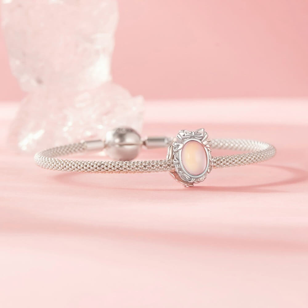 Sterling silver mirror charm with iridescent center and ornate bow frame.