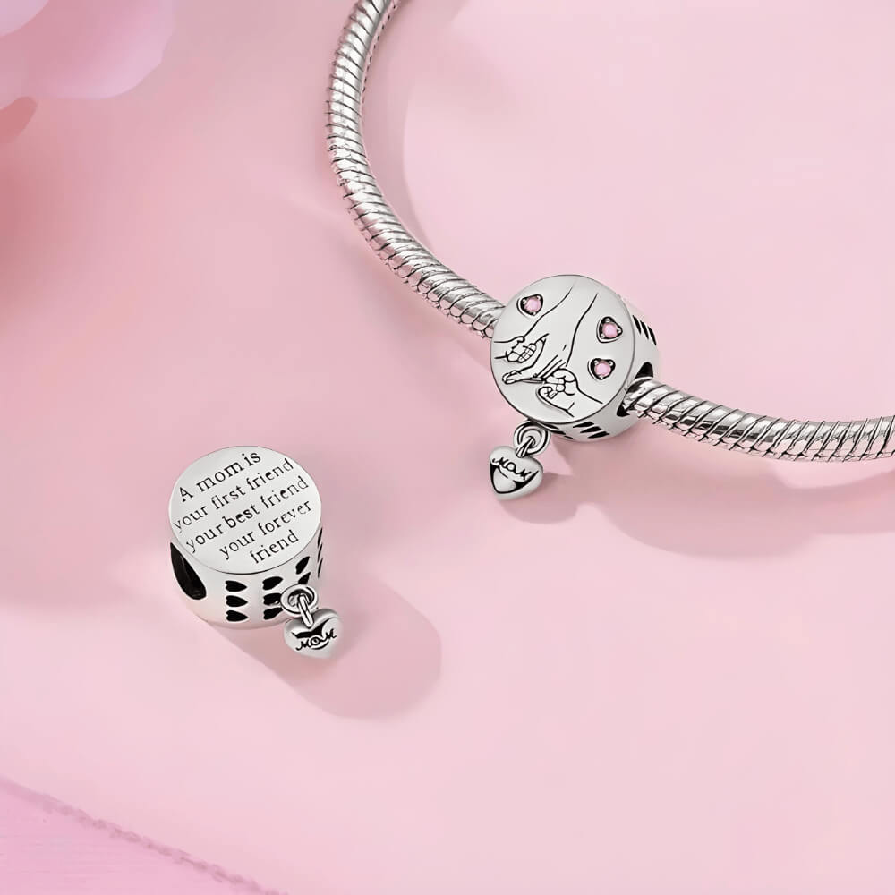 Sterling silver round charm with engraved mother and child hands, pink crystal hearts, and dangling ‘Mom’ tag 