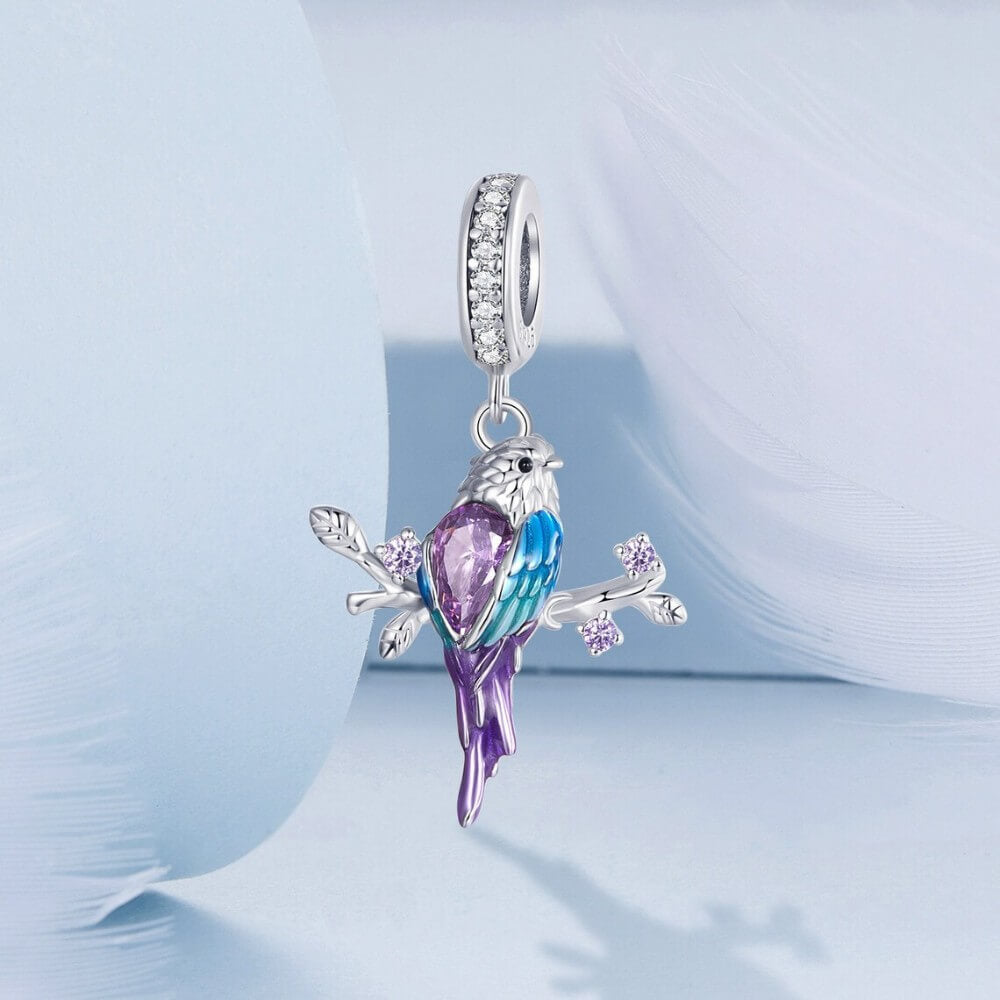 Sterling silver parrot charm with purple crystal, blue enamel, and branch details.