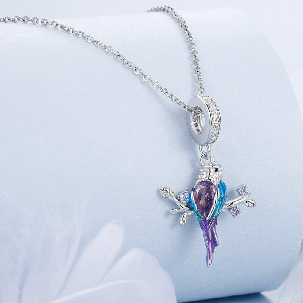 Bird-shaped pendant with purple and blue colors on a chain against a light blue background