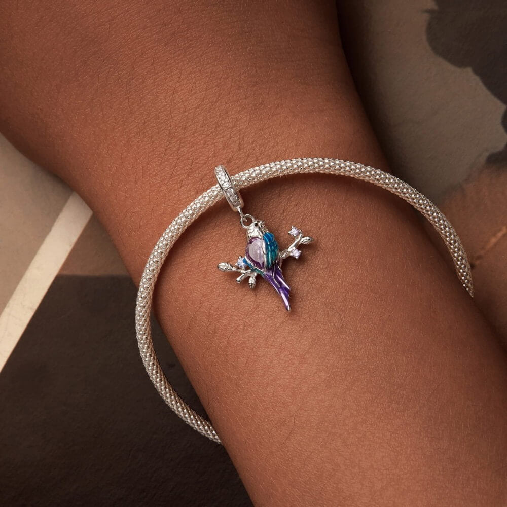 Sterling silver parrot charm with purple crystal, blue enamel, and branch details.