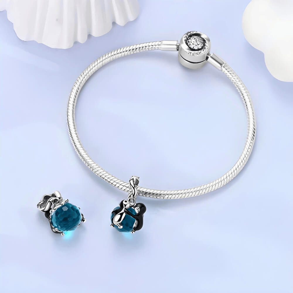 Sterling silver penguin couple charm with blue faceted crystal and star-detailed bail.