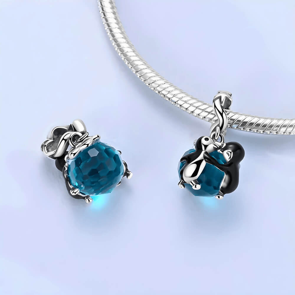 Sterling silver penguin couple charm with blue faceted crystal and star-detailed bail.