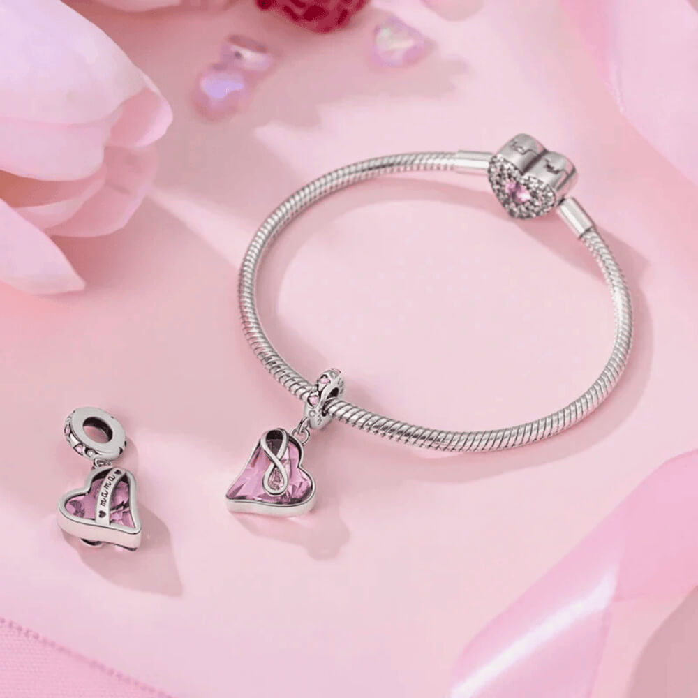 Sterling silver dangle charm with a faceted light-pink crystal heart wrapped in an infinity symbol and pink heart stones on the bail