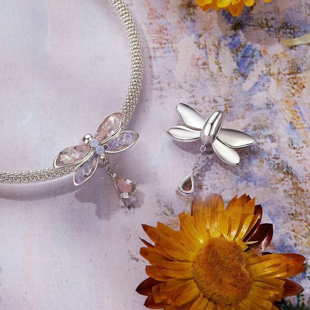 Silver dragonfly necklace with gemstones on a textured surface with flowers.