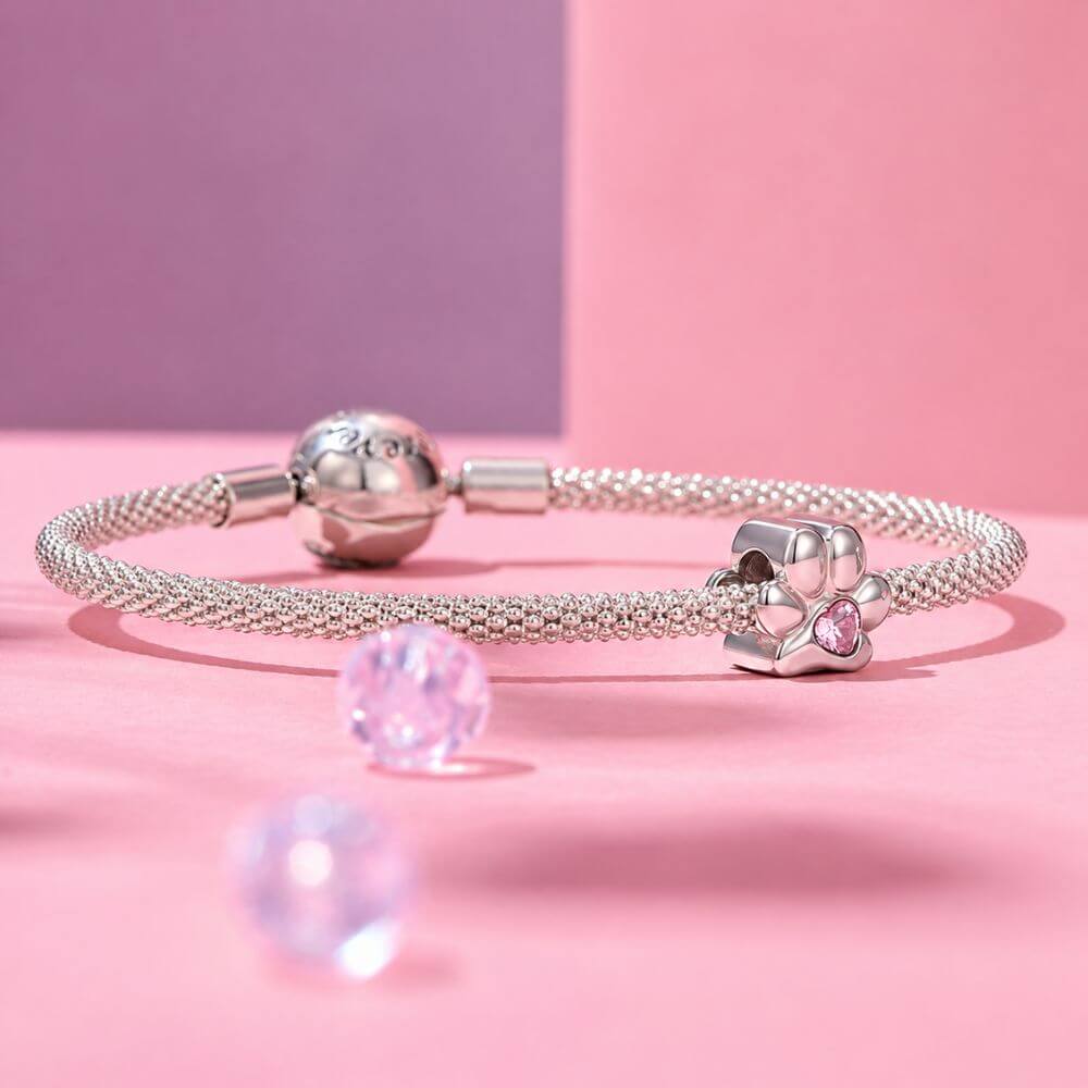 Sterling silver paw print charm with pink heart crystal center and polished pet-inspired details.