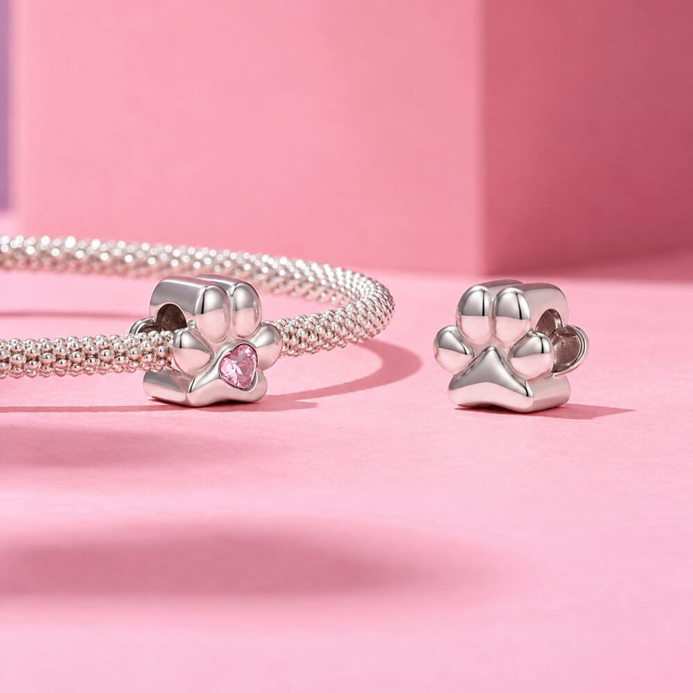 Sterling silver paw print charm with pink heart crystal center and polished pet-inspired details.