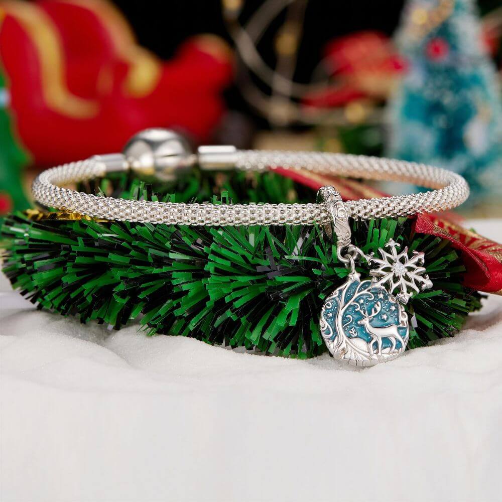 Sterling silver reindeer charm with blue enamel heart, snowflake dangle, stars, and winter forest details.