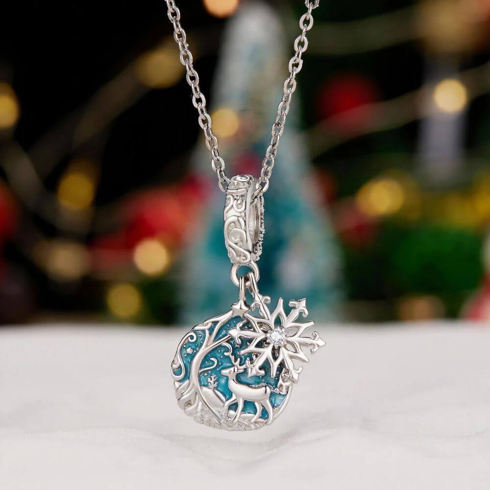 Sterling silver reindeer charm with blue enamel heart, snowflake dangle, stars, and winter forest details.