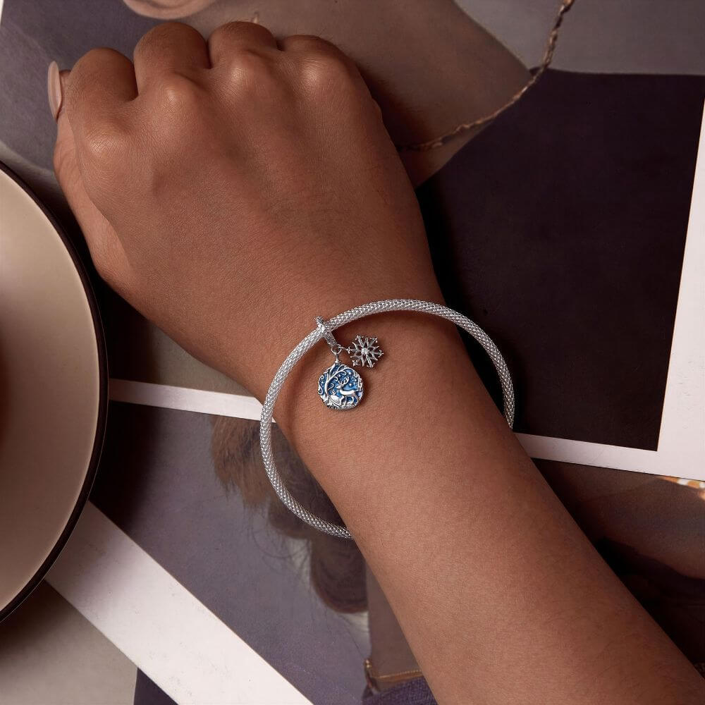 Sterling silver reindeer charm with blue enamel heart, snowflake dangle, stars, and winter forest details.