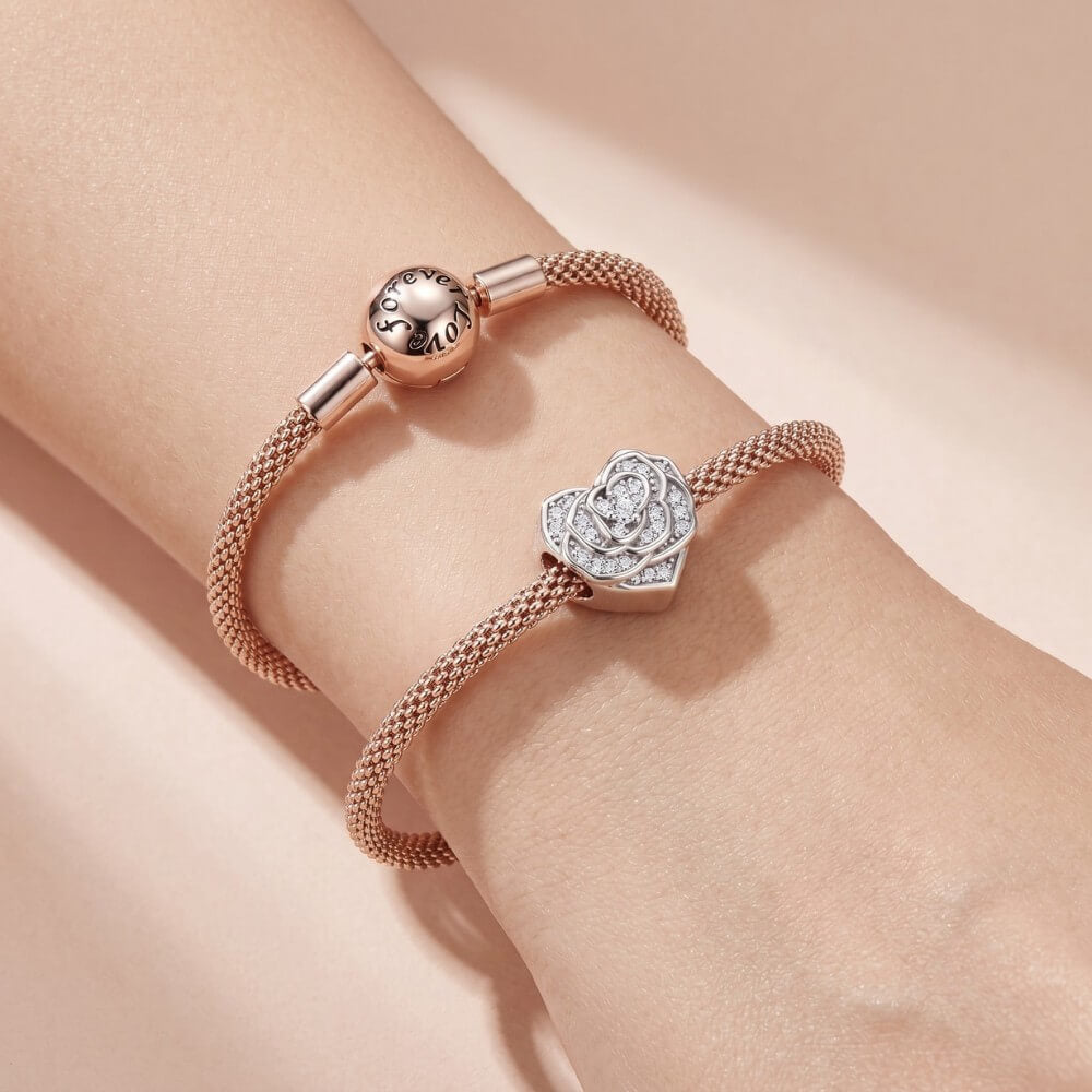 Rose gold bracelet with a rose and heart-shaped charm on a wrist against a beige background