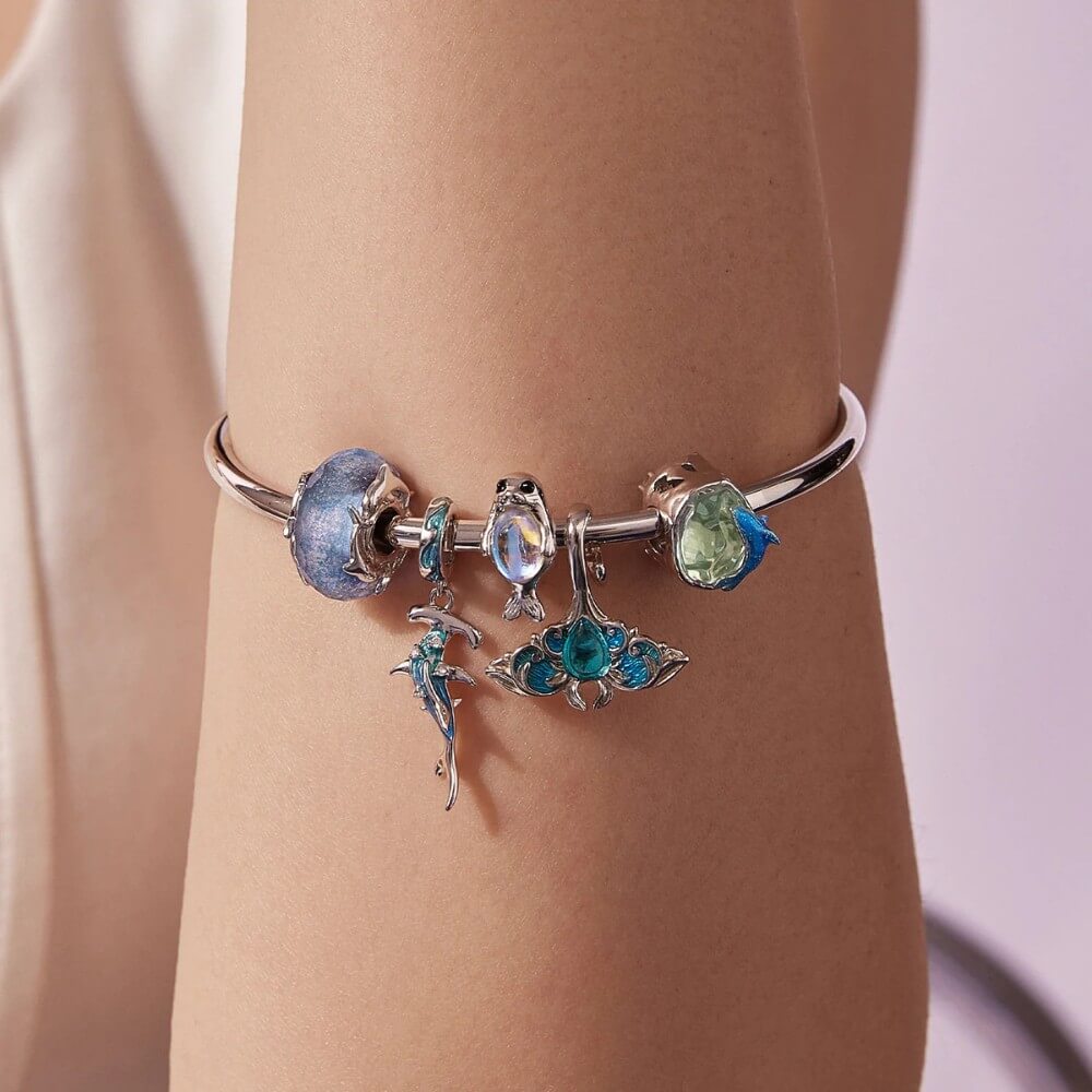 Silver bracelet with blue and green charms on a wrist against a neutral background