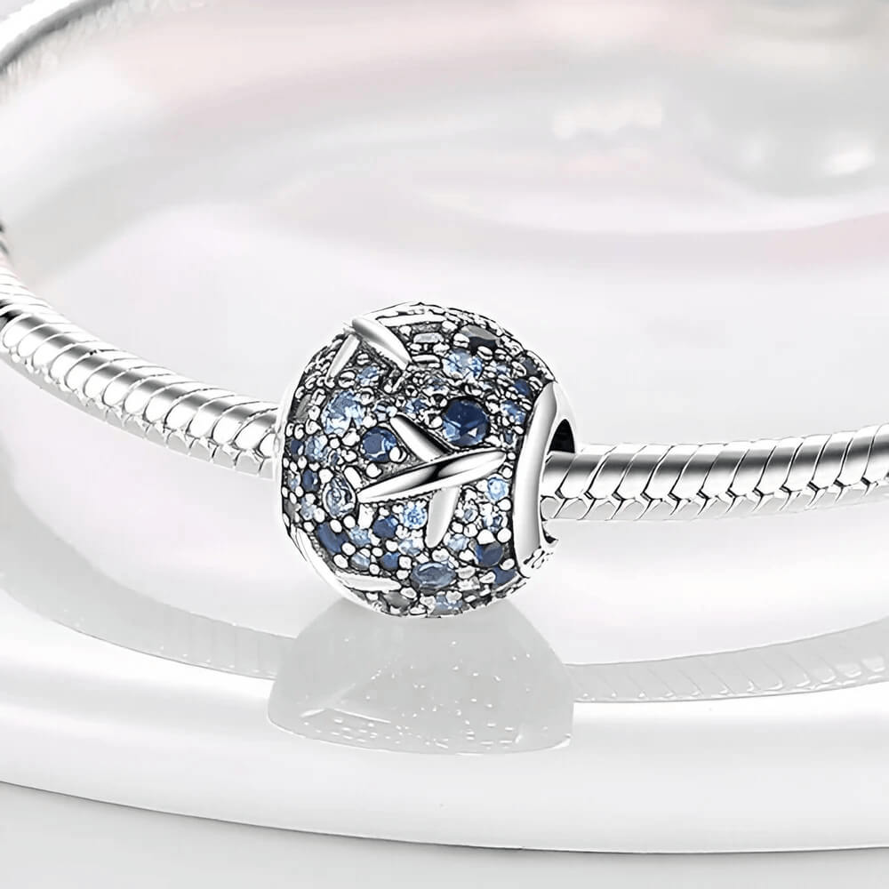 Sterling silver charm covered in light and dark blue stones with raised airplane motifs across the surface 