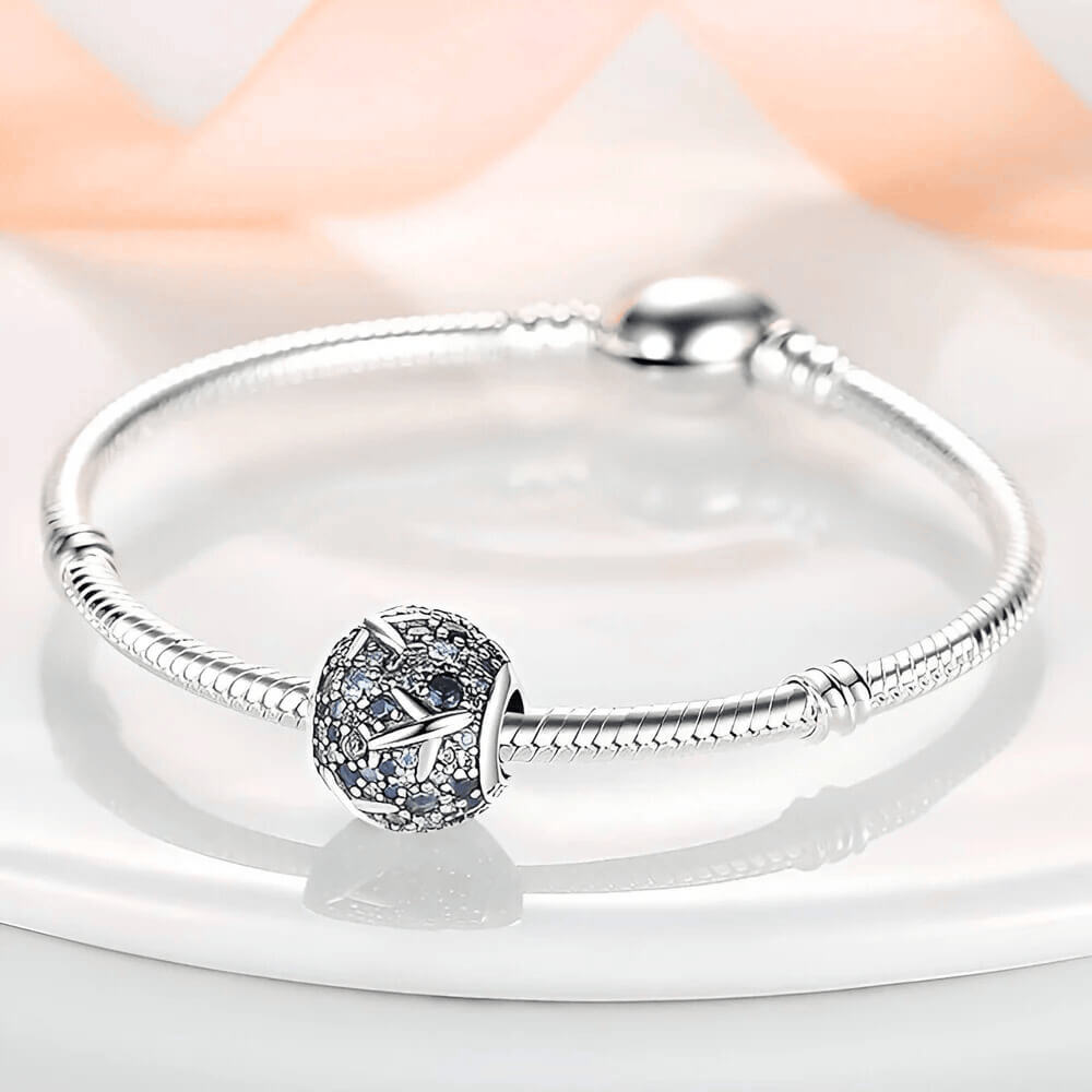 Sterling silver charm covered in light and dark blue stones with raised airplane motifs across the surface 