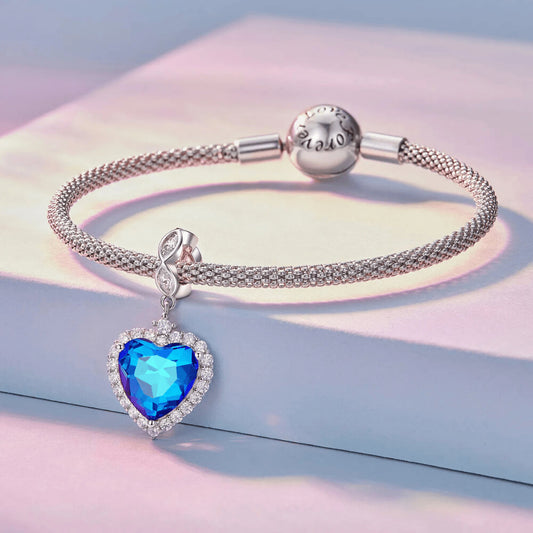 Sterling silver charm with a large faceted blue heart crystal framed by clear stones and a decorative bail set with clear marquise crystals 