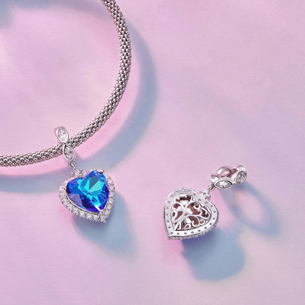Sterling silver charm with a large faceted blue heart crystal framed by clear stones and a decorative bail set with clear marquise crystals 