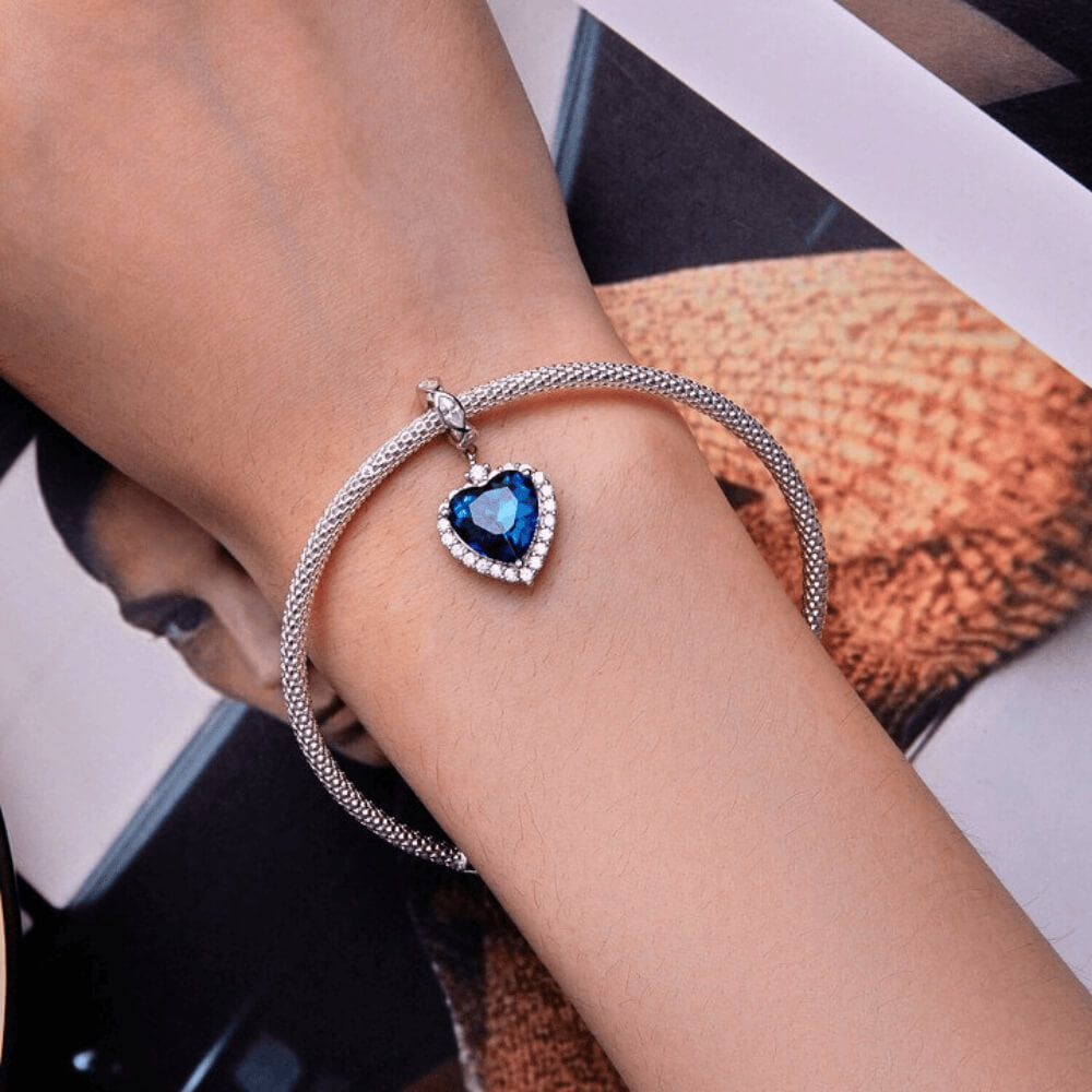 Sterling silver charm with a large faceted blue heart crystal framed by clear stones and a decorative bail set with clear marquise crystals 