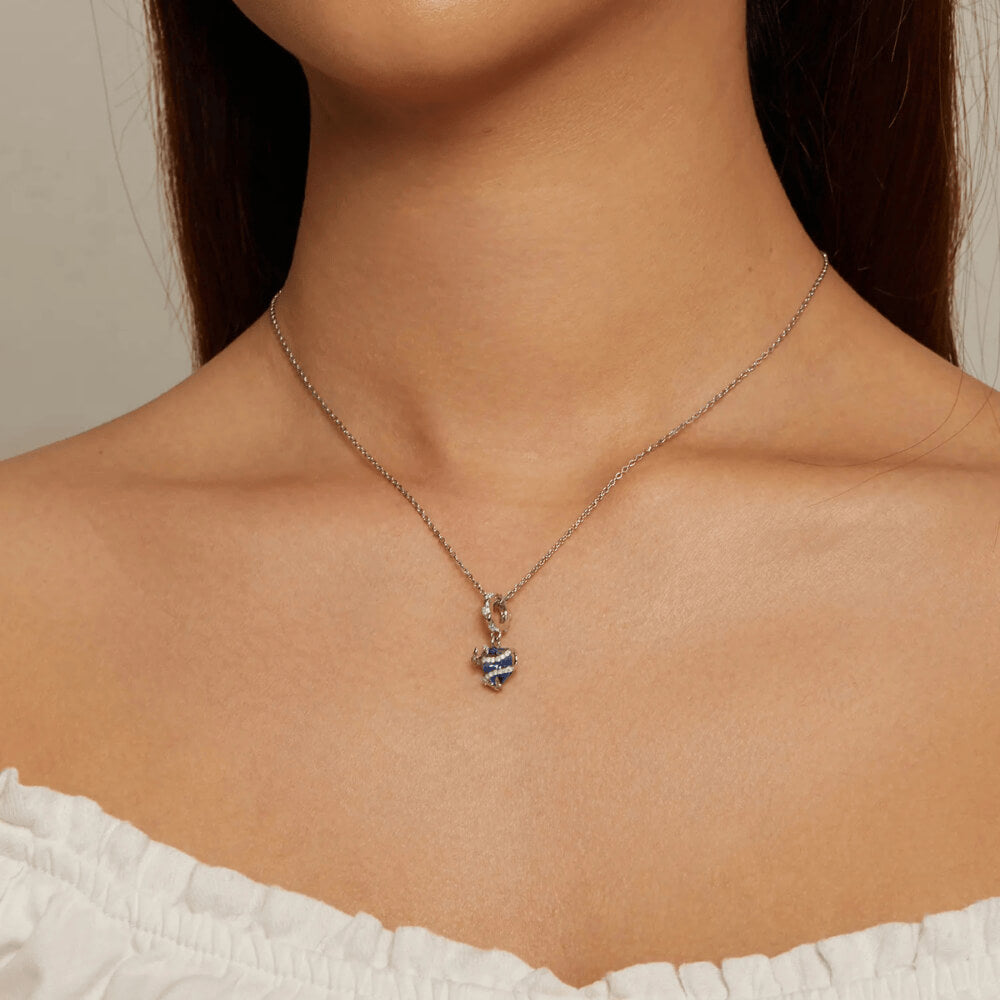 Sterling silver charm with a bright blue faceted heart crystal wrapped in silver vine-like details and small round light-blue stones on the bail 