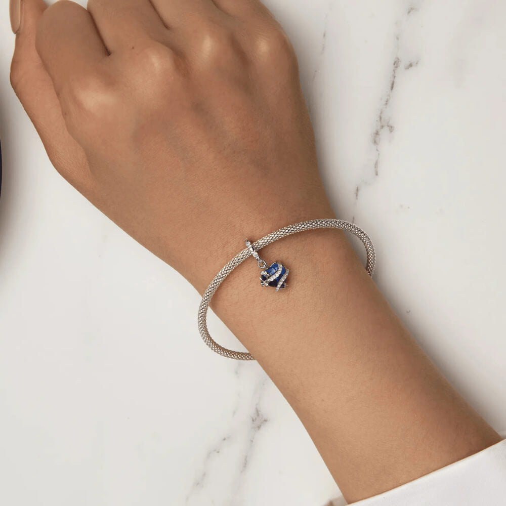 Sterling silver charm with a bright blue faceted heart crystal wrapped in silver vine-like details and small round light-blue stones on the bail 