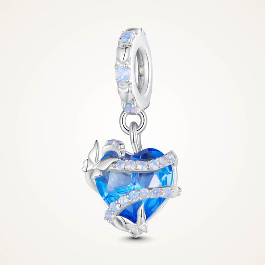 Sterling silver charm with a bright blue faceted heart crystal wrapped in silver vine-like details and small round light-blue stones on the bail – ORÉYA.