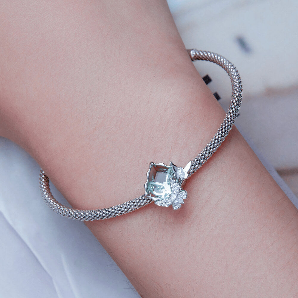 Sterling silver charm with a large pale green faceted stone and two crystal-studded silver butterflies on the front 