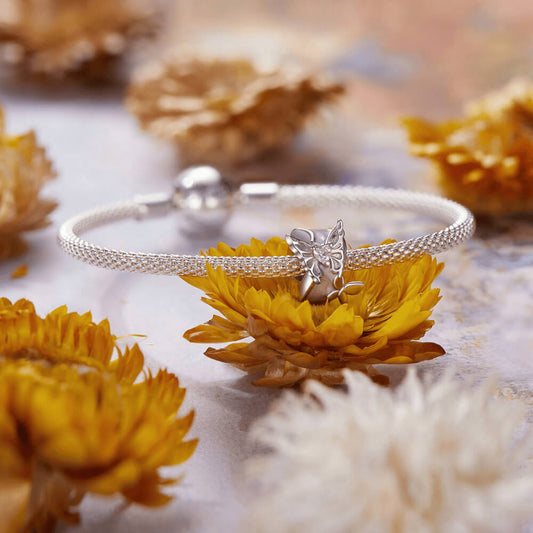 Sterling silver charm with a pale pink enamel background, a silver butterfly with a pink heart-shaped stone, and an additional silver flower detail 