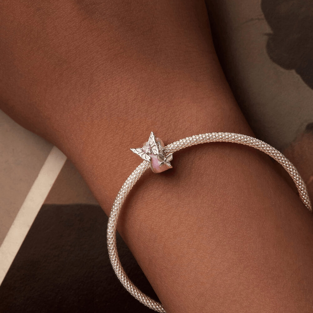 Sterling silver charm with a pale pink enamel background, a silver butterfly with a pink heart-shaped stone, and an additional silver flower detail