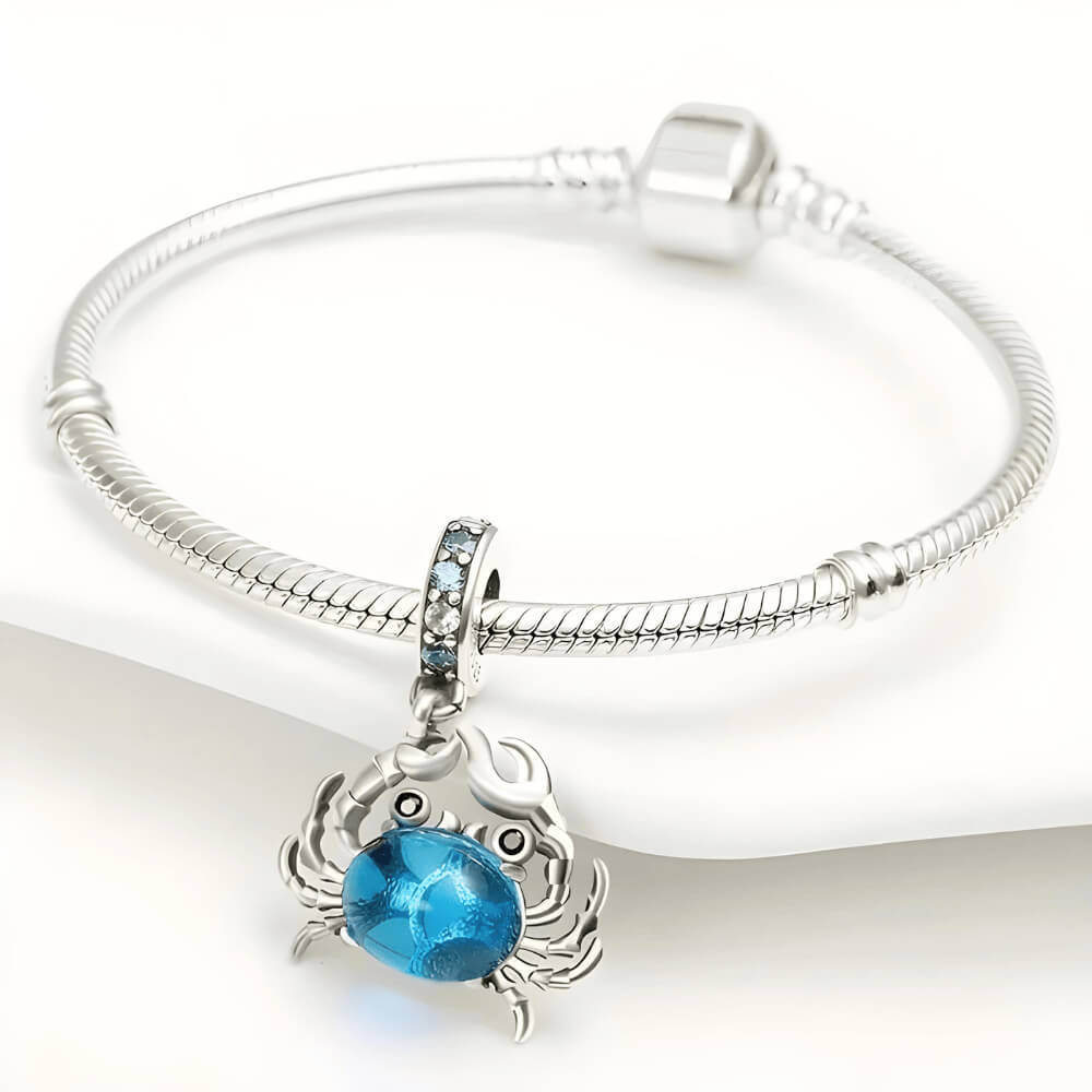 Sterling silver crab charm with a large blue oval stone body, black stone eyes, and a bail decorated with light-blue crystals