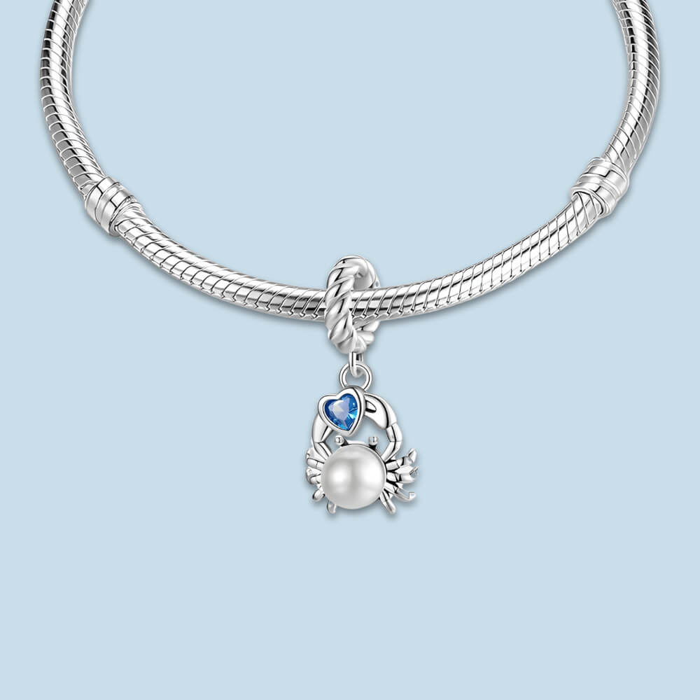 Sterling silver crab charm with a large white pearl-like body and a blue heart-shaped stone, on a twisted silver bail 