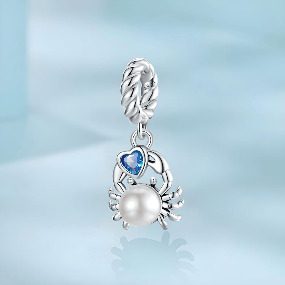 Sterling silver crab charm with a large white pearl-like body and a blue heart-shaped stone, on a twisted silver bail 
