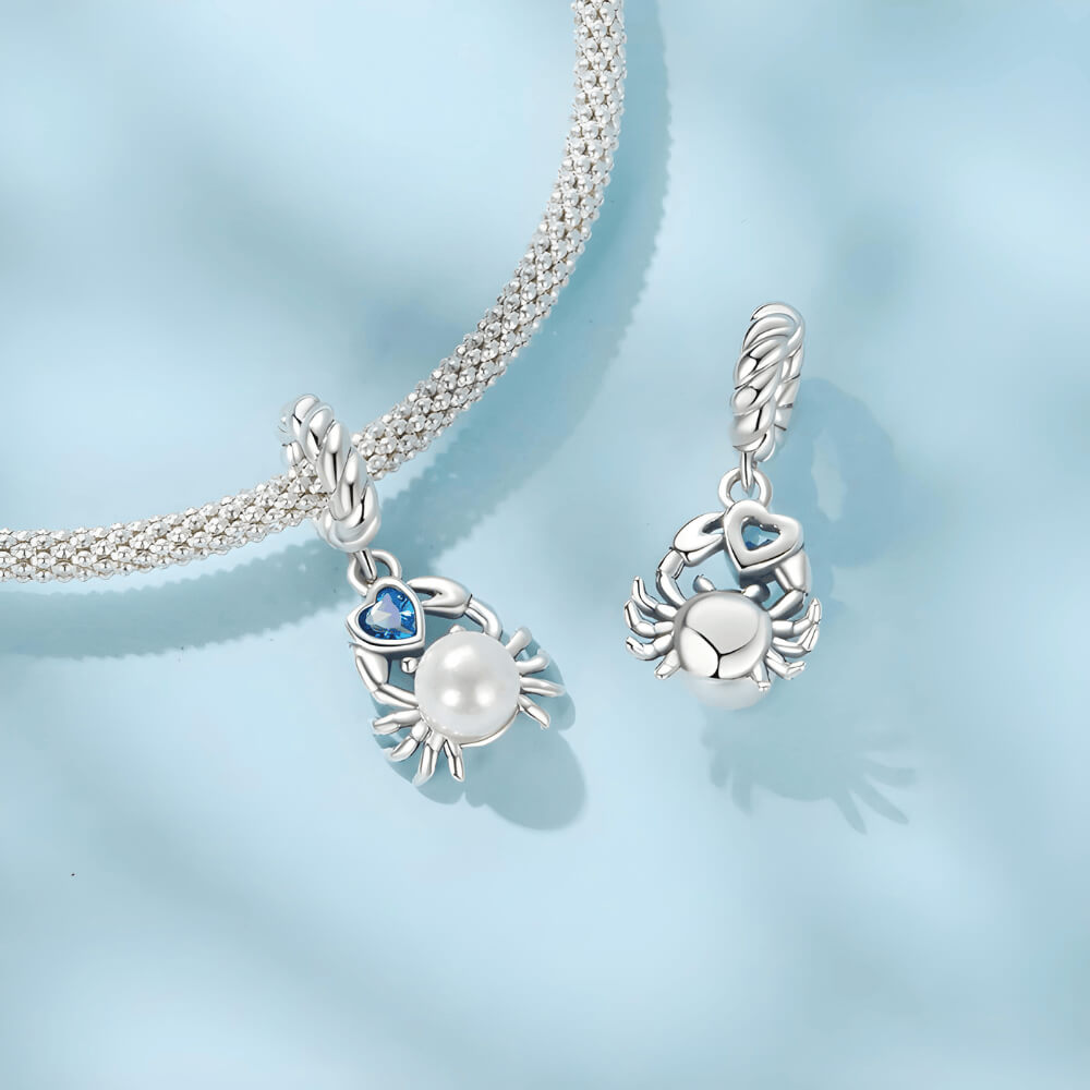 Sterling silver crab charm with a large white pearl-like body and a blue heart-shaped stone, on a twisted silver bail