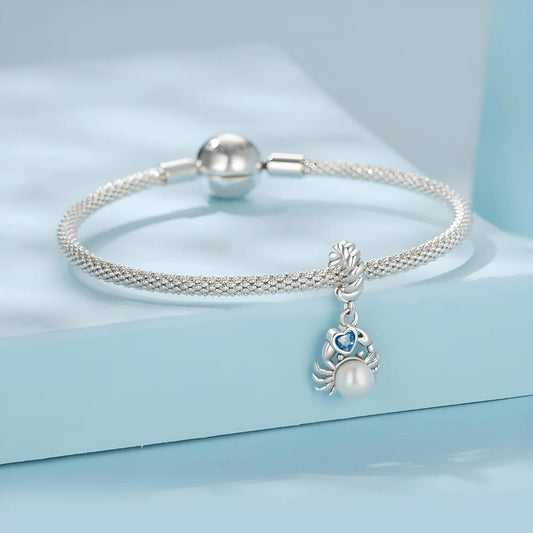 Sterling silver crab charm with a large white pearl-like body and a blue heart-shaped stone, on a twisted silver bail