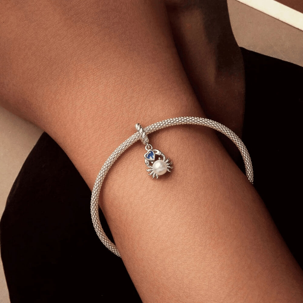 Sterling silver crab charm with a large white pearl-like body and a blue heart-shaped stone, on a twisted silver bail 