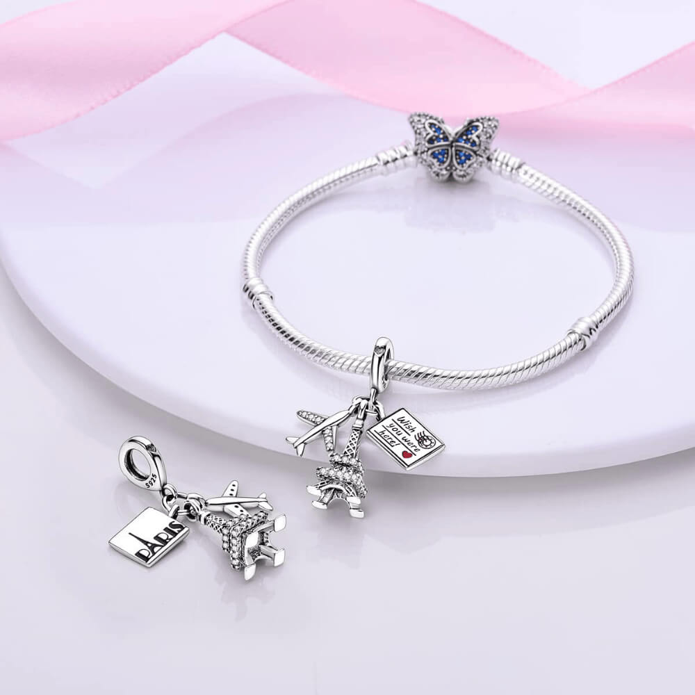 Sterling silver charm with a crystal-studded Eiffel Tower, a small airplane with clear stones, and an engraved postcard 