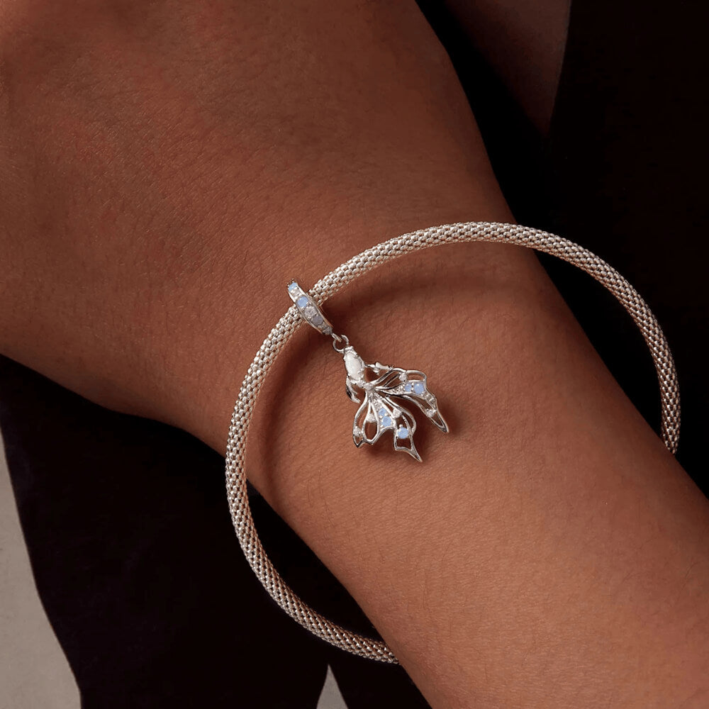 Sterling silver fish charm with opal-like stone and blue gemstone accents.