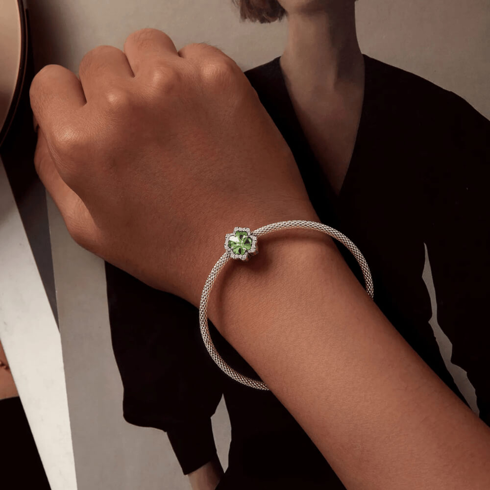 Sterling silver charm with a large green four-petal faceted stone framed by clear crystals 