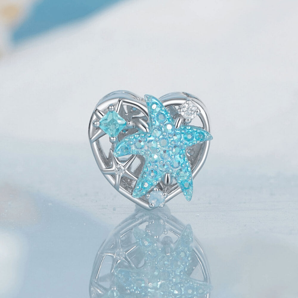 Sterling silver heart-shaped charm with a large blue crystal starfish, light-blue and clear stones, and an openwork background 