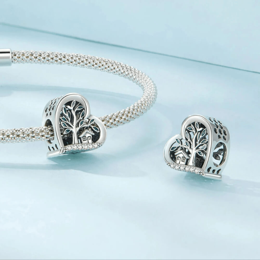 Sterling silver heart-shaped charm with a green-enamel tree, small house detail, and a row of clear crystals along the bottom 
