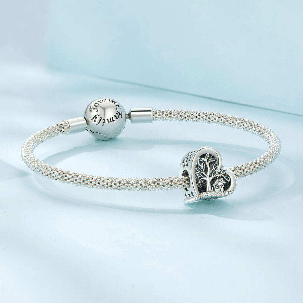 Sterling silver heart-shaped charm with a green-enamel tree, small house detail, and a row of clear crystals along the bottom