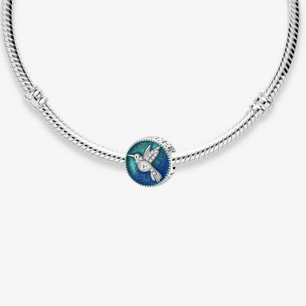 Sterling silver round charm with a crystal-studded hummingbird over a blue and teal enamel background with floral engravings