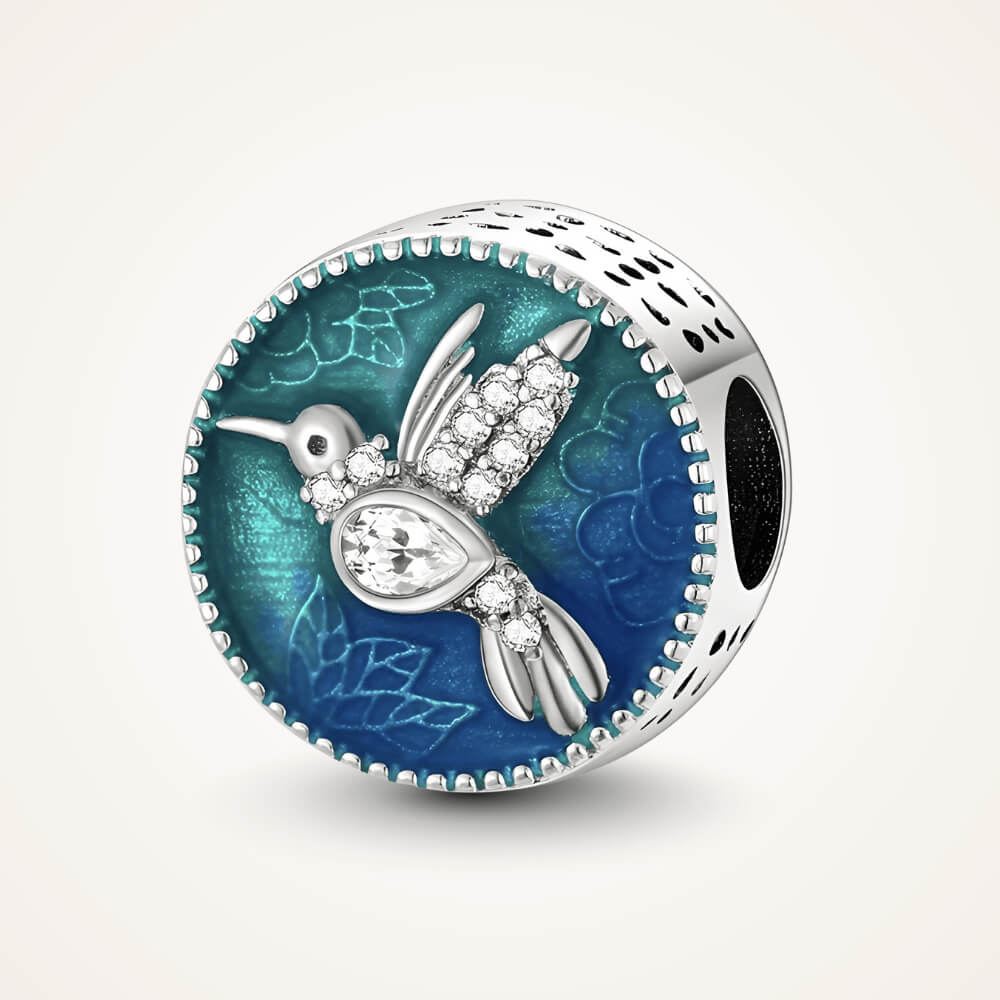 Sterling silver round charm with a crystal-studded hummingbird over a blue and teal enamel background with floral engravings – ORÉYA.