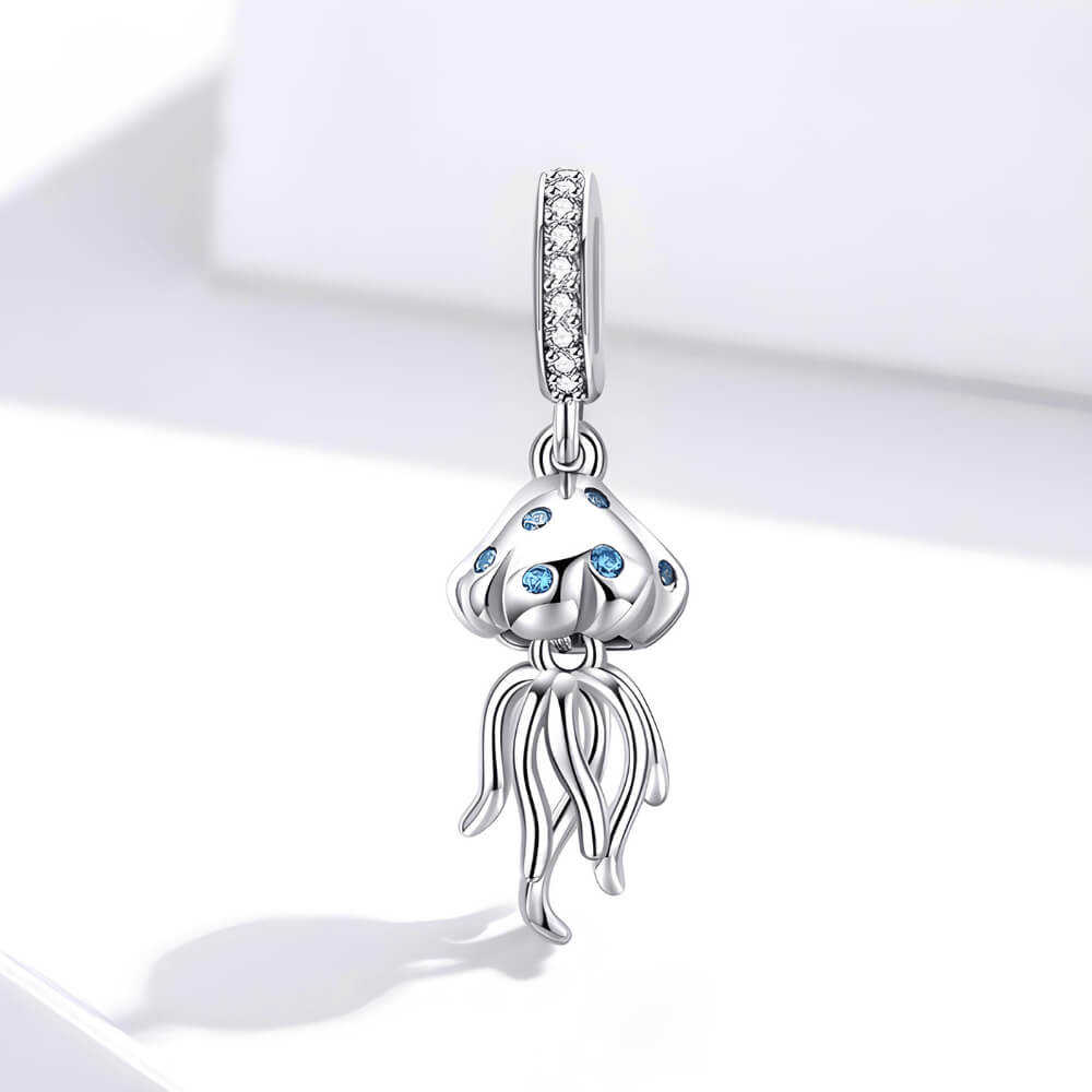 Sterling silver jellyfish charm with blue stones on the bell and long flowing tentacles, hanging from a bail set with clear crystals